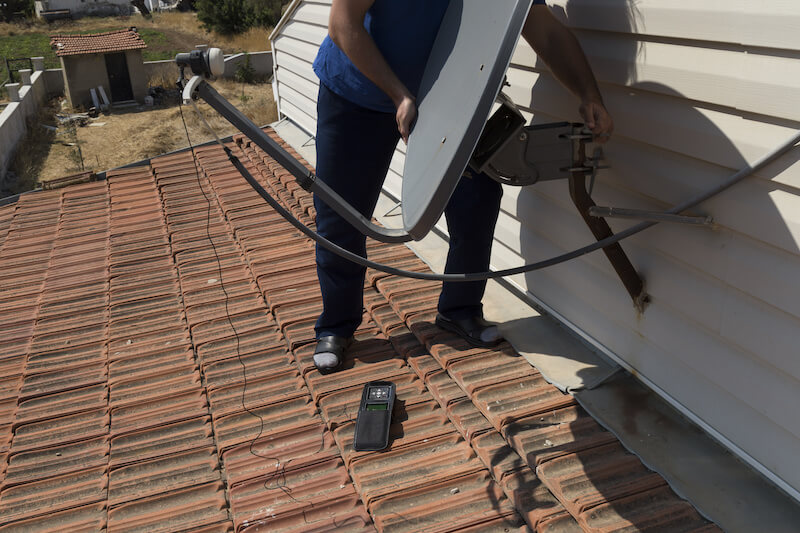 屋根上でパラボラアンテナを固定する男性